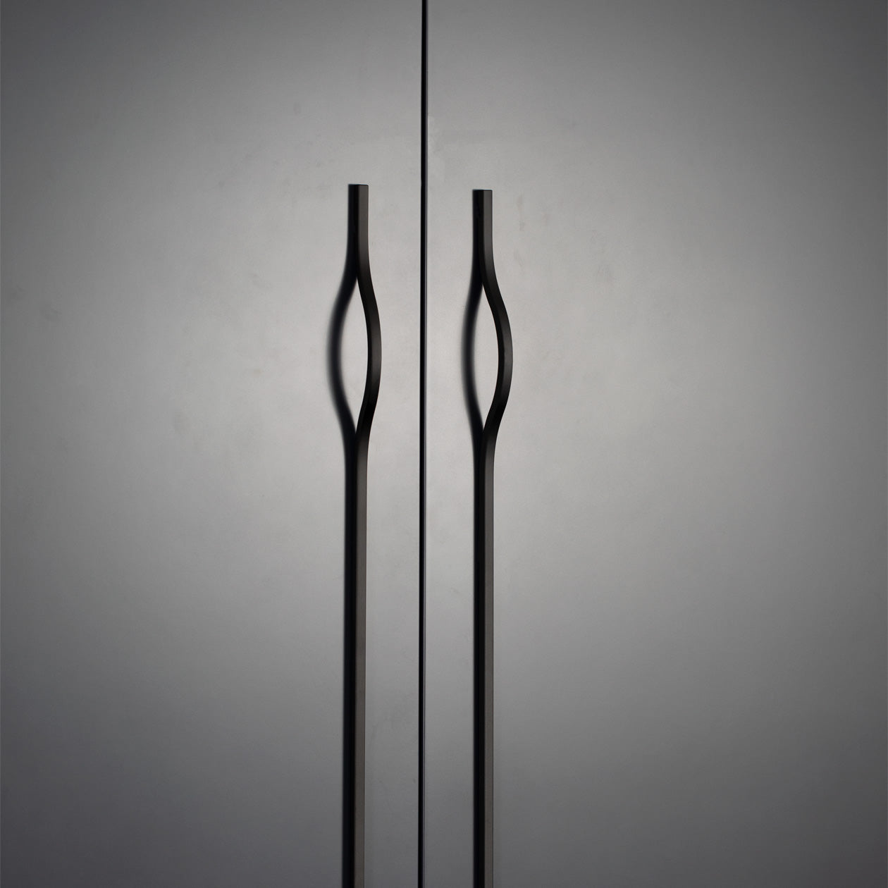 Momo BRAVE Bow off-centred cabinet pull handle in matte black finish mounted on a wooden cabinet door.