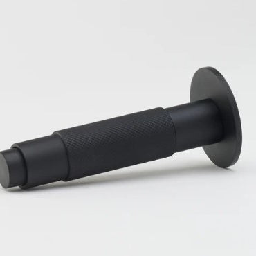 Lo & Co Interiors knurled Kintore doorstop in brushed metal finish, resting on a wooden floor.
