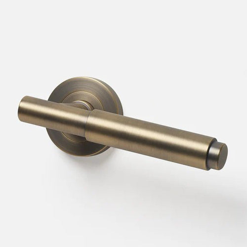Lo & Co Lola Lever door handle in antique brass finish, featuring a sleek lever design on a white door.