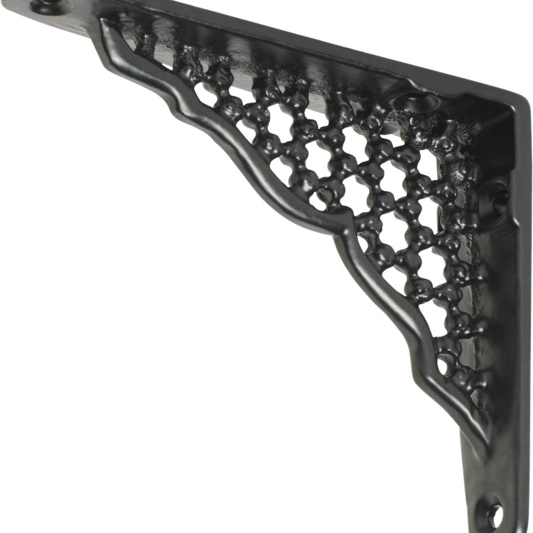 Decorative Tradco ornate shelf bracket in black with intricate scrollwork, mounted on a wooden shelf for support.