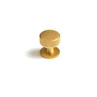 Momo Belgravia knurled cabinet knob in brushed brass finish mounted on a wooden cabinet door.
