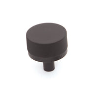 Momo Bellevue knurled cabinet knob in matte black with textured grip, mounted on a wooden cabinet door.